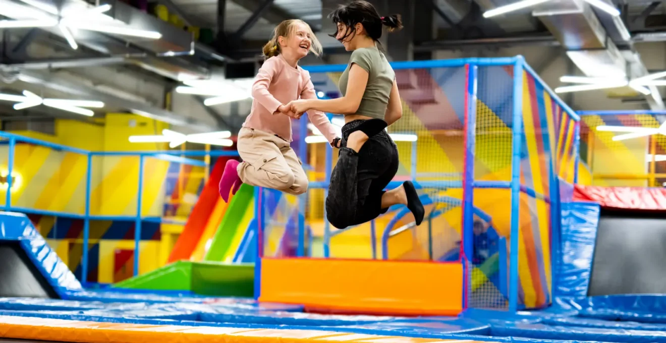 Des enfants sautent ensemble sur les trampolines d'un parc intérieur sous la surveillance d'un animateur.