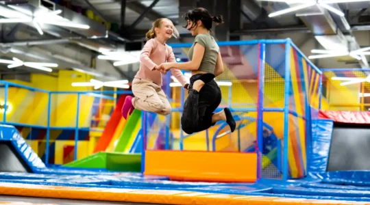 Des enfants sautent ensemble sur les trampolines d'un parc intérieur sous la surveillance d'un animateur.